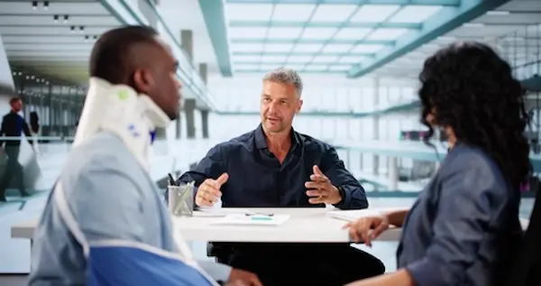 client with a neck brace and his partner sitting with a personal injury lawyer discussing how their case will be handled by a team like H Groves Law LLC.